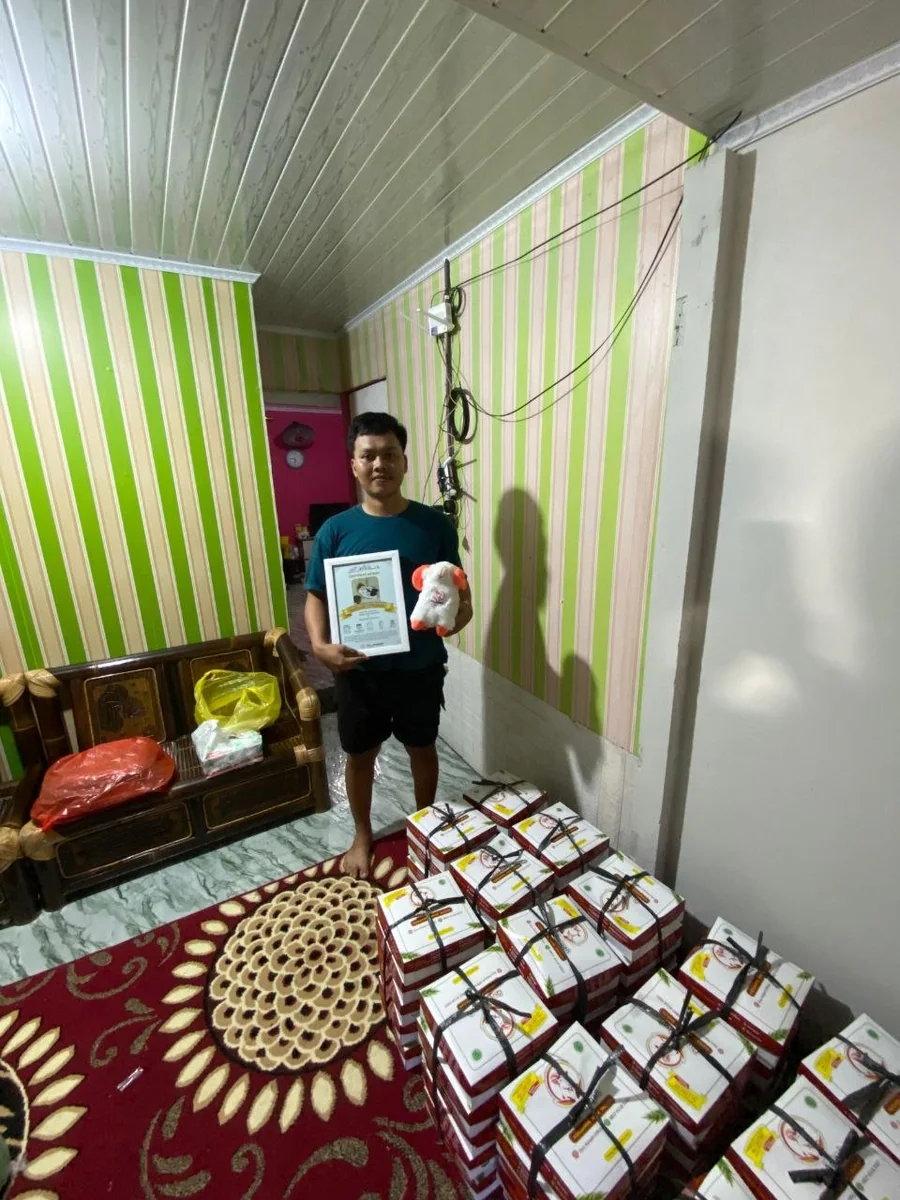 Pelanggan memegang sertifikat dan boneka di samping box pesanan Quy