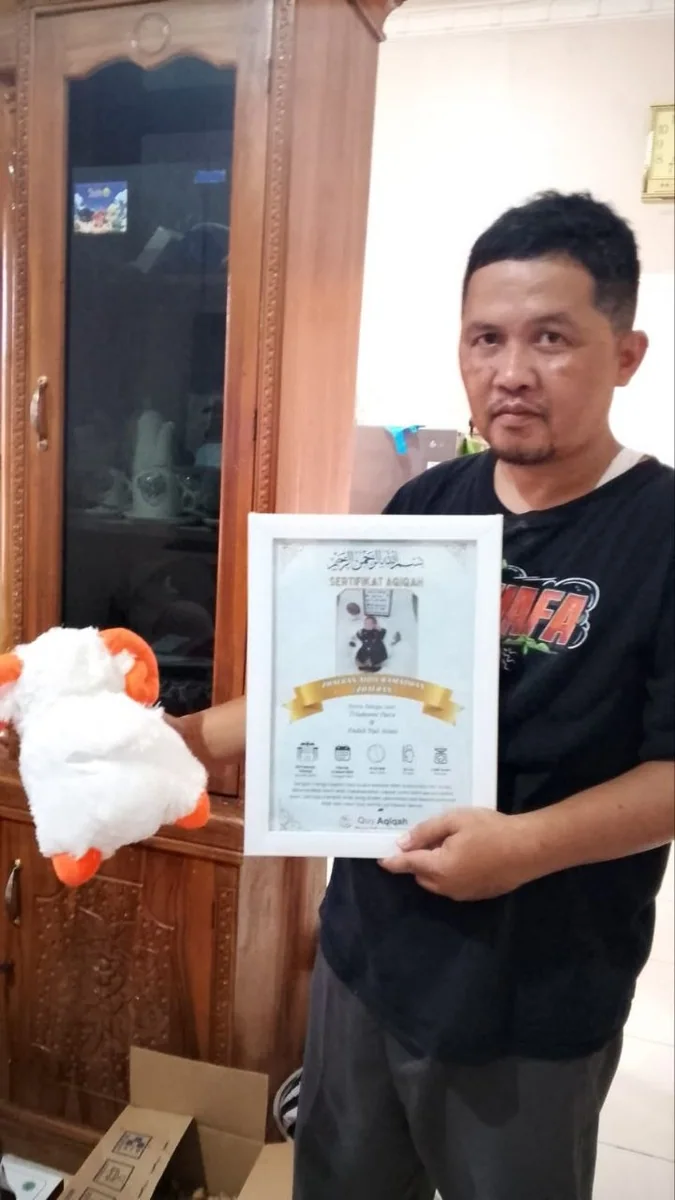 Pelanggan Quy memegang sertifikat aqiqah dan boneka suvenir