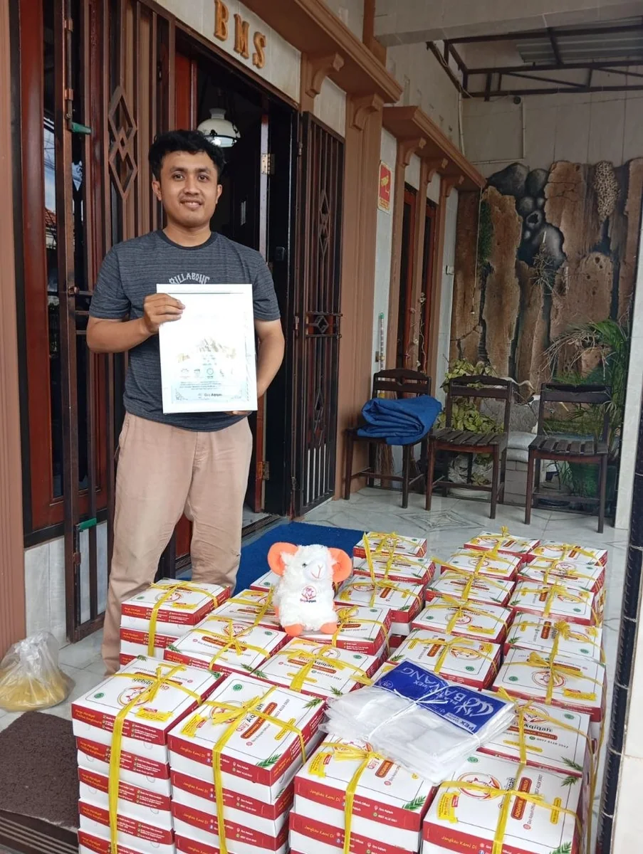 Pelanggan Quy berdiri di depan rumah dengan sertifikat dan tumpukan box pesanan